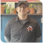 Man in dark polo shirt and cap standing in front of shelves with potted plants