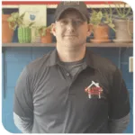 Man in dark polo shirt and cap standing in front of shelves with potted plants