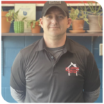 Man in dark polo shirt and cap standing in front of shelves with potted plants