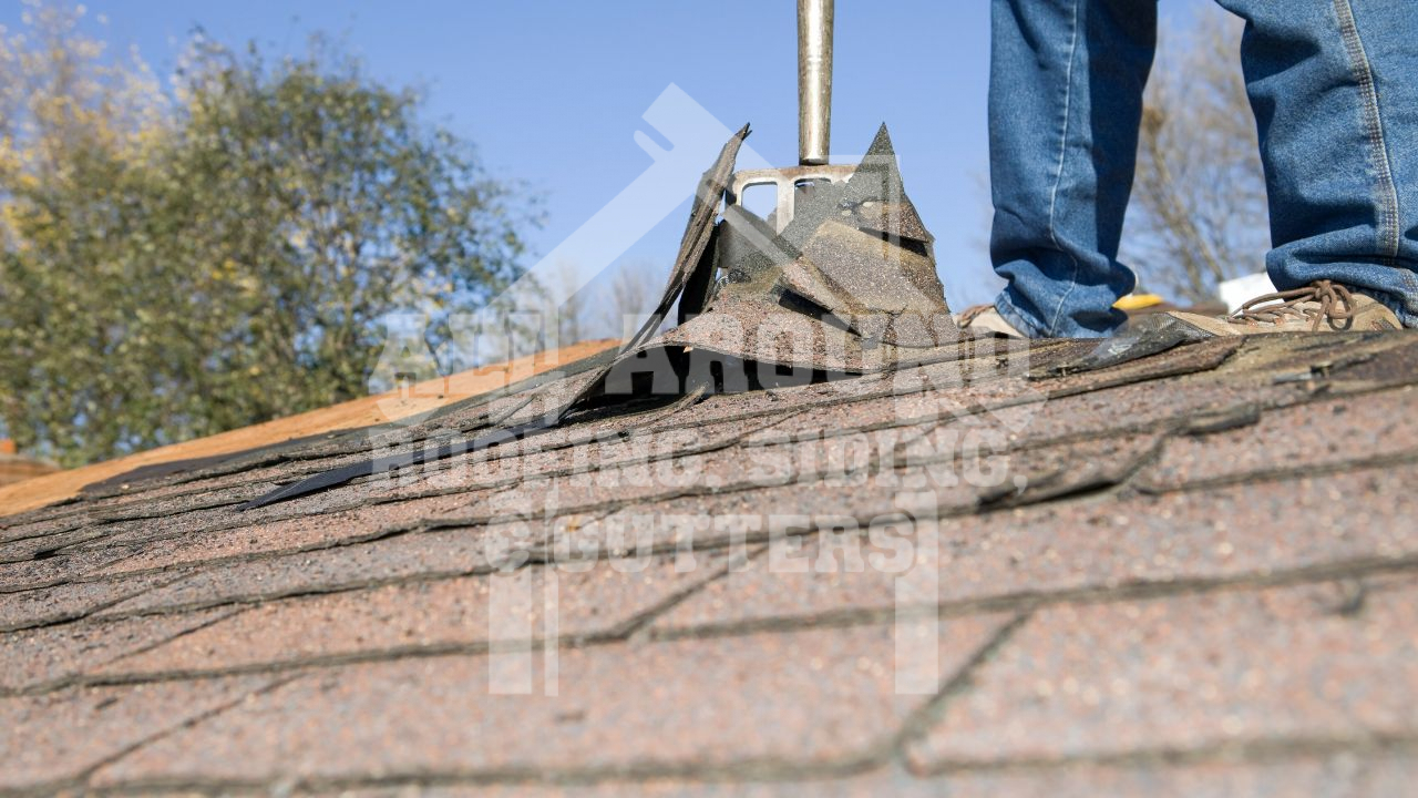 Roofer installing shingles on residential roof with tools and equipment visible