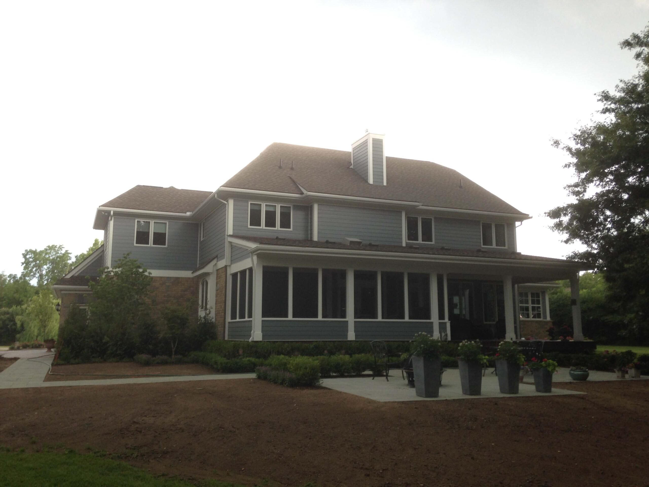 Two-story gray house with wraparound porch and white chimney in residential setting