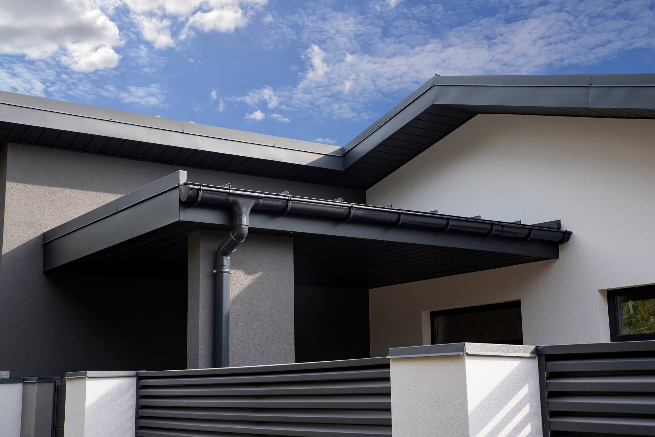 Modern house exterior with dark gutters and downspout against blue cloudy sky