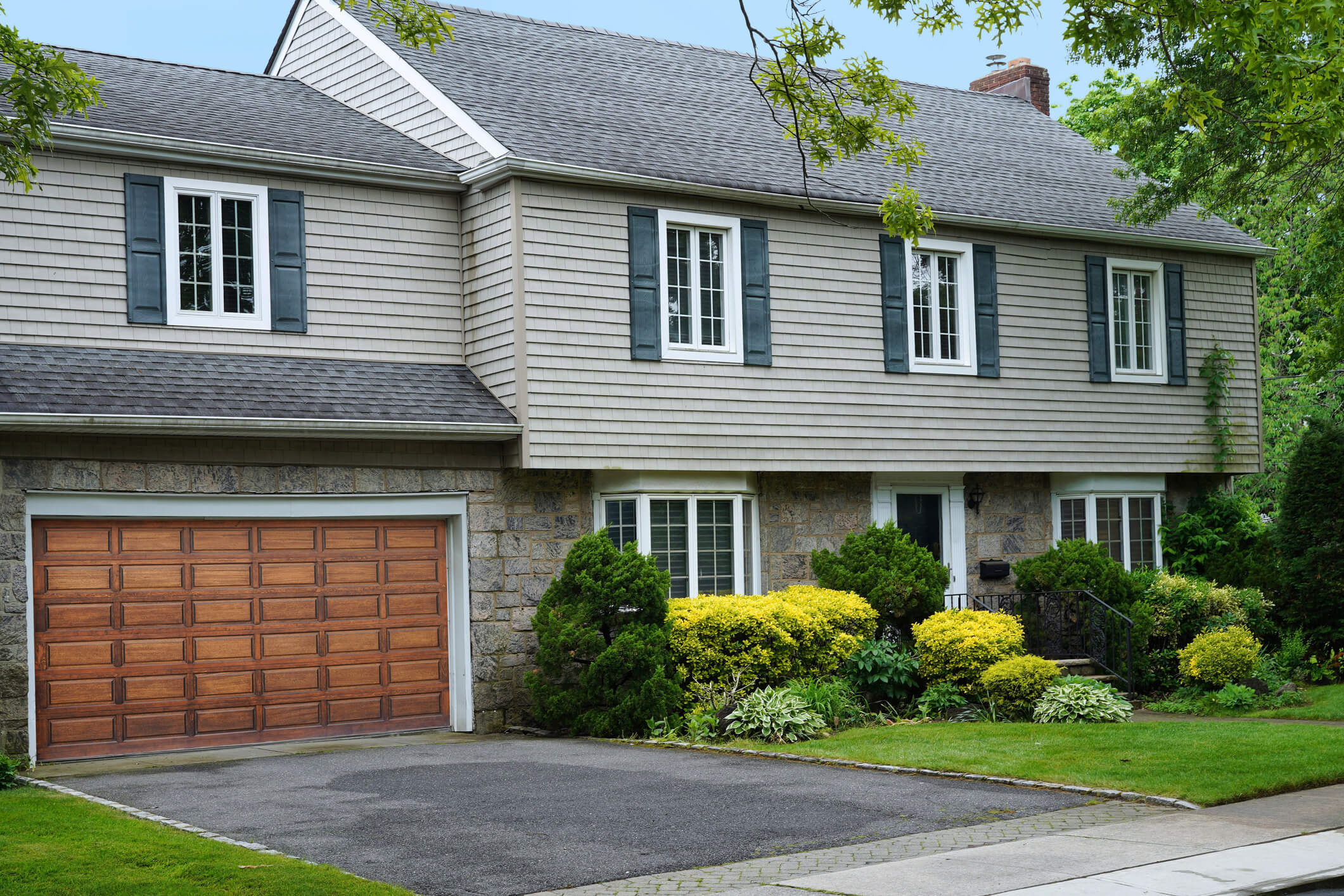 Two-story suburban home with beige siding, blue shutters, and wooden garage door