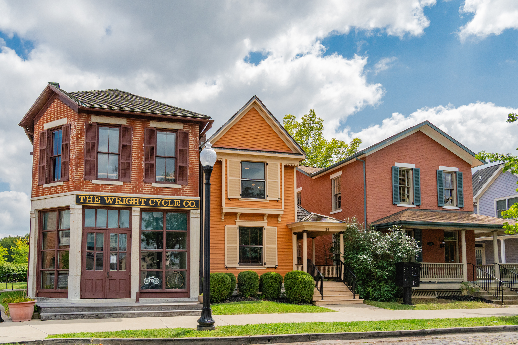 Historic Wright Cycle Co. brick building with colorful Victorian houses on tree-lined street