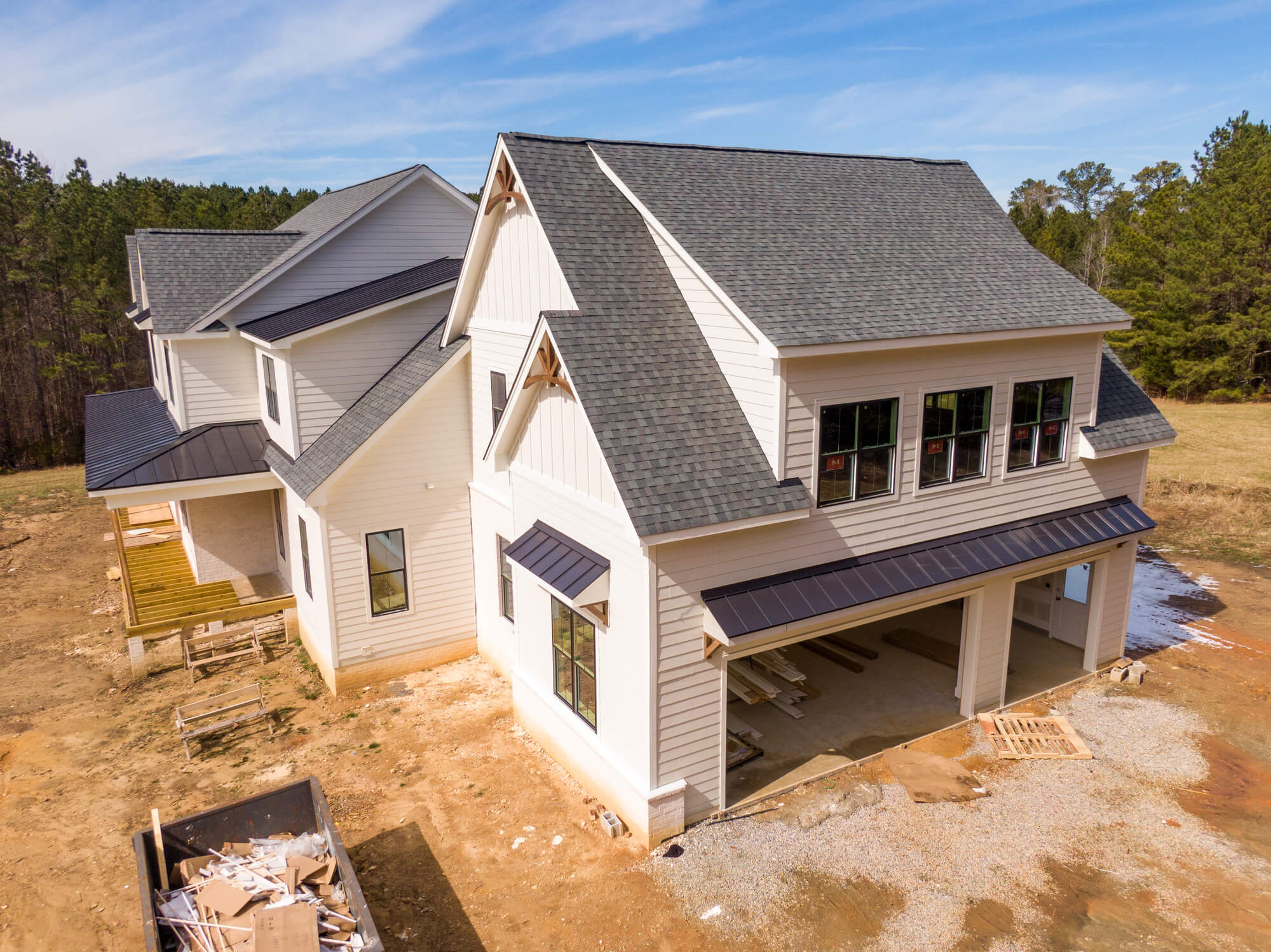 Modern white farmhouse under construction with gray shingle roof and attached garage