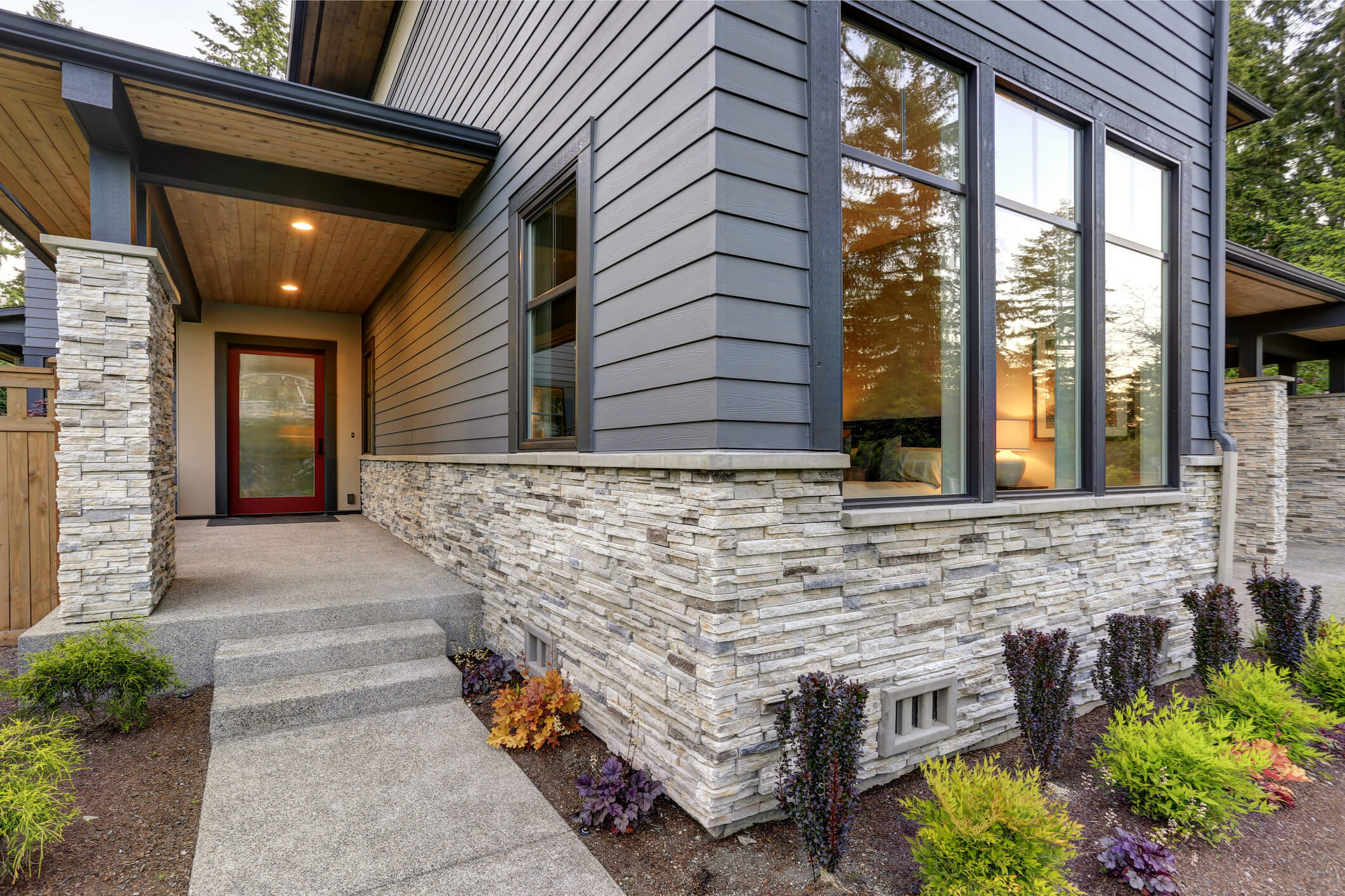 Modern home exterior with gray siding, stone foundation, and large windows
