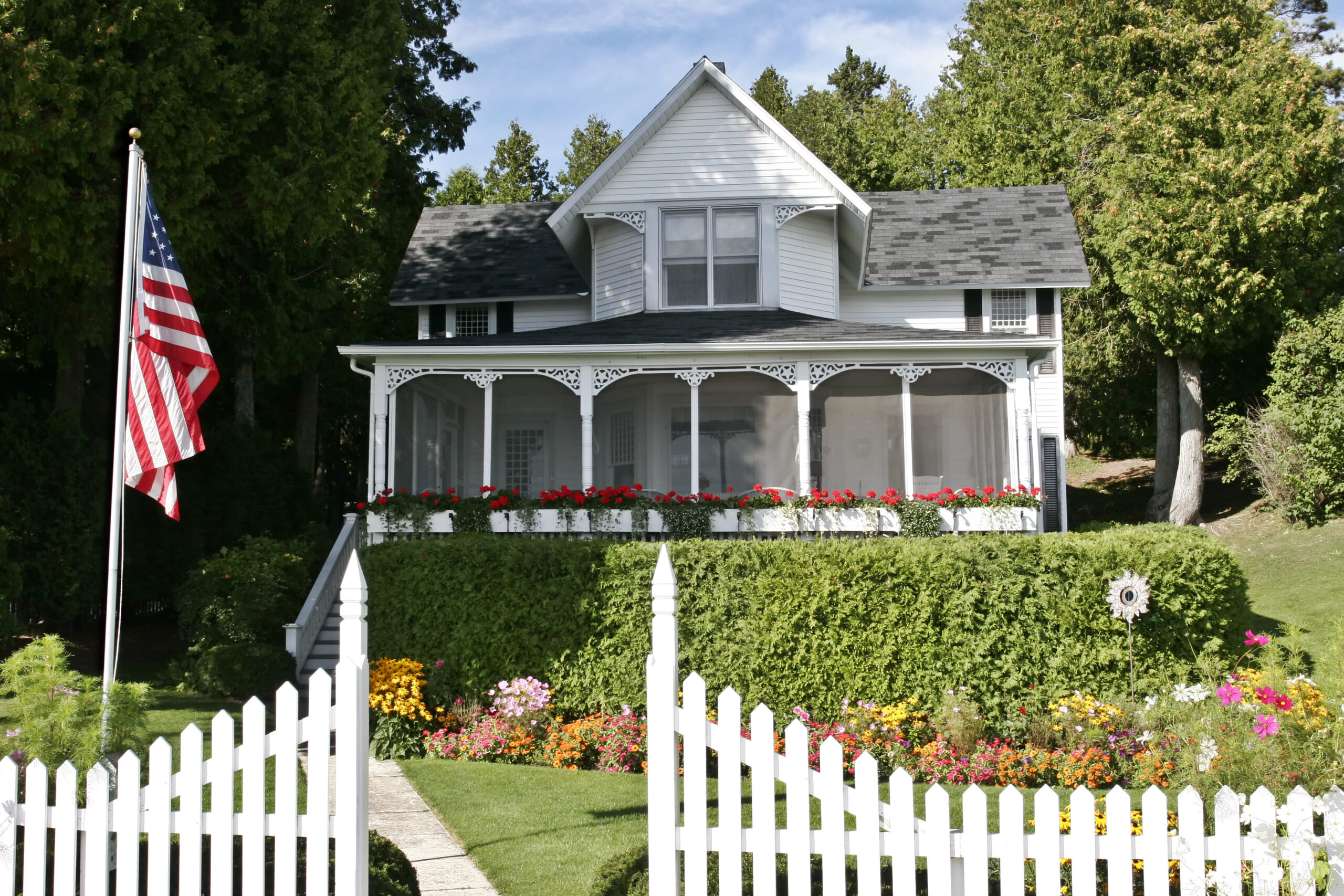 White Victorian house with wraparound porch, decorative trim, and American flag