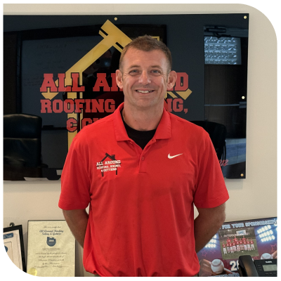 Smiling person in a red shirt standing in front of a company sign.